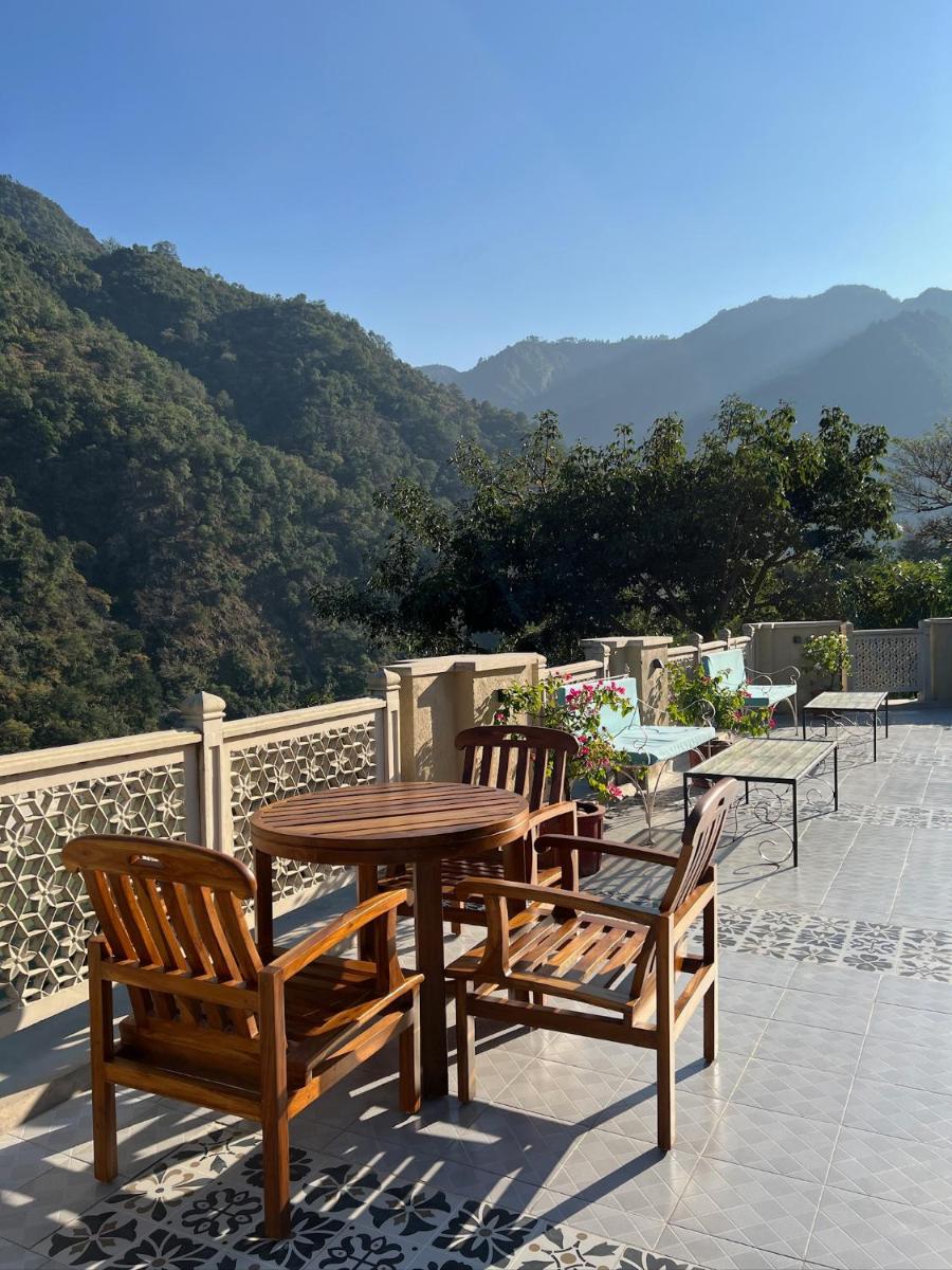 a wooden table and chairs on a patio with mountains at Raga on the Ganges, Rishikesh in Rishīkesh