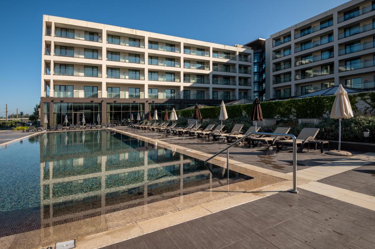 uma piscina com cadeiras e guarda-sóis em frente a um prédio em Vila Gale Coimbra em Coimbra