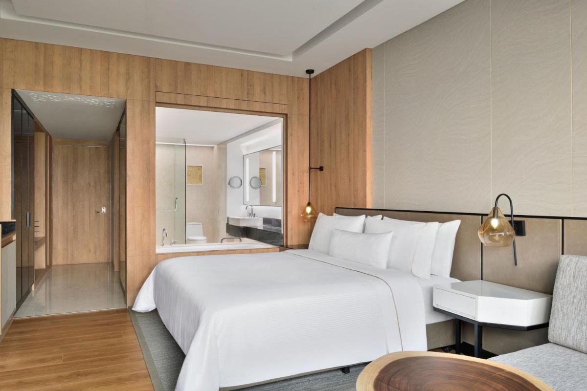 a bedroom with a large white bed and a chair at The Westin Mumbai Powai Lake in Mumbai