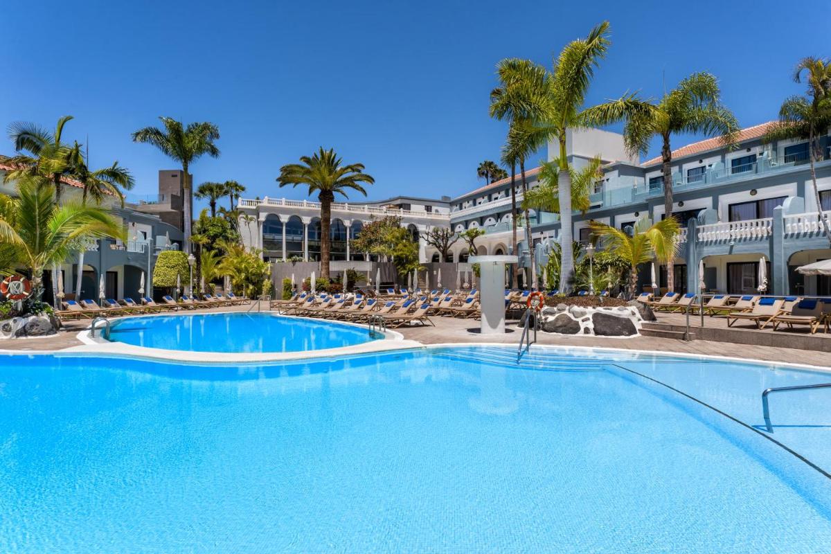 Una gran piscina en un complejo con palmeras. en Adrián Hoteles Colón Guanahaní Adultos Only, en Adeje
