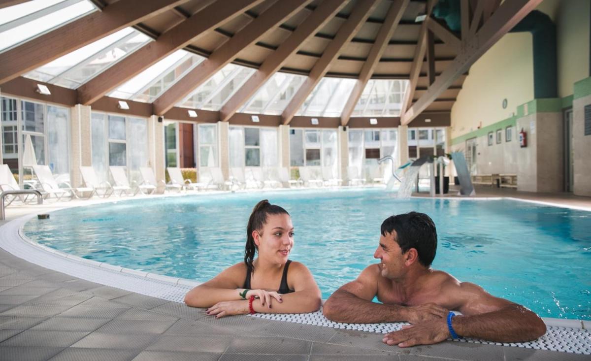 Un hombre y una mujer tumbados en una piscina en Lobios Caldaria Hotel Balneario, en Bubaces