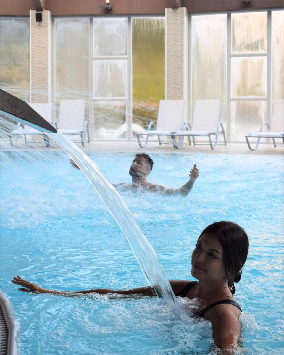 un hombre y una mujer en una piscina con una fuente en Lobios Caldaria Hotel Balneario, en Bubaces