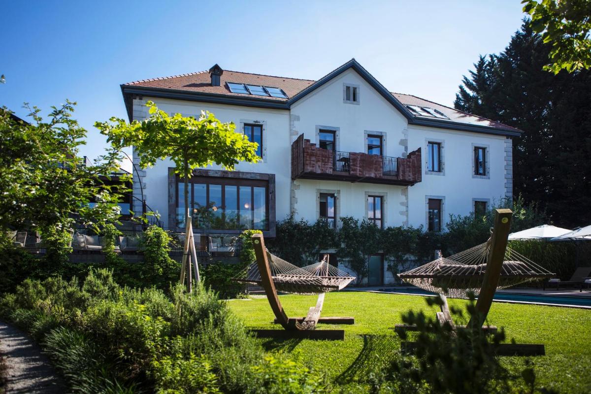 une grande maison blanche avec des hamacs en face de celle-ci dans l'établissement Le Clos Des Sens, à Annecy