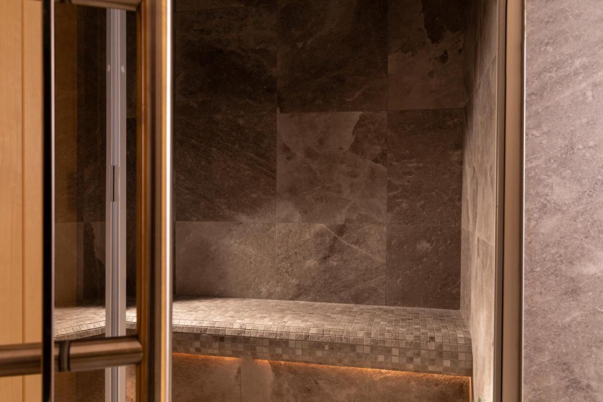 une porte de douche en verre avec un banc à l'intérieur dans l'établissement Hôtel Le Lavoisier & Spa, à Paris