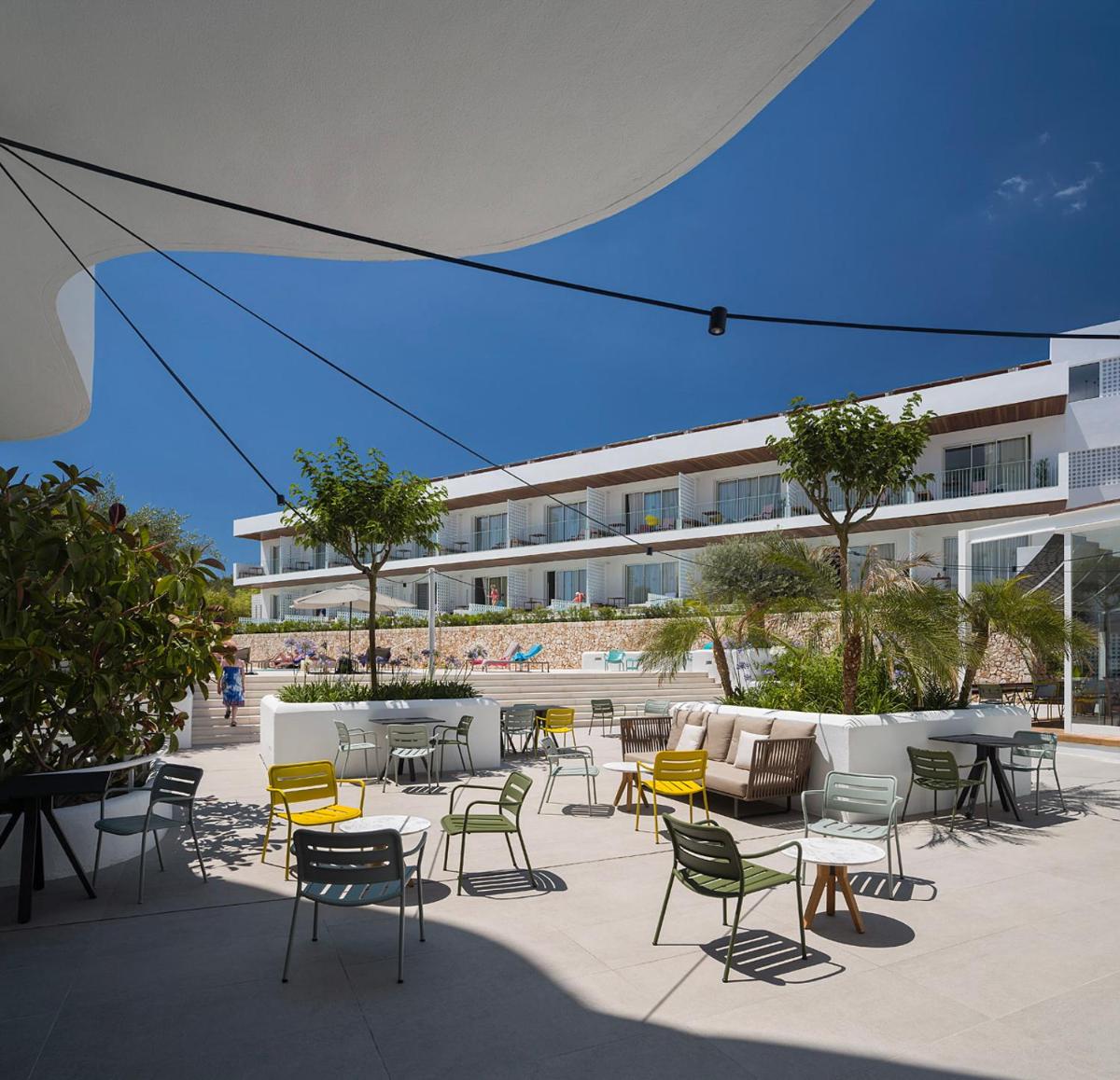 Un patio con sillas y mesas y un edificio. en Inturotel Cala Esmeralda Beach Hotel & Spa - Adults Only, en Cala d´Or