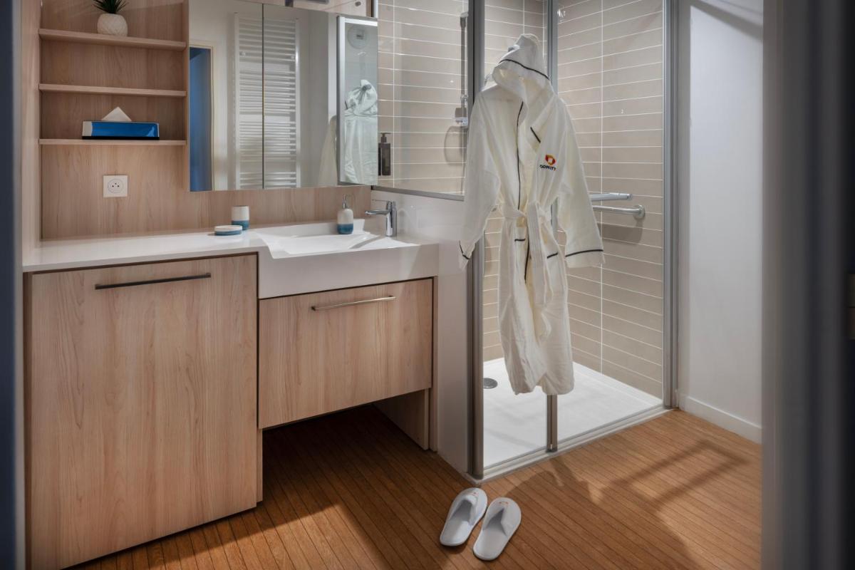 une salle de bain avec un lavabo et une douche avec un peignoir dans l'établissement DOMITYS L'ALLIACEE - Résidence Services Séniors, à Achères