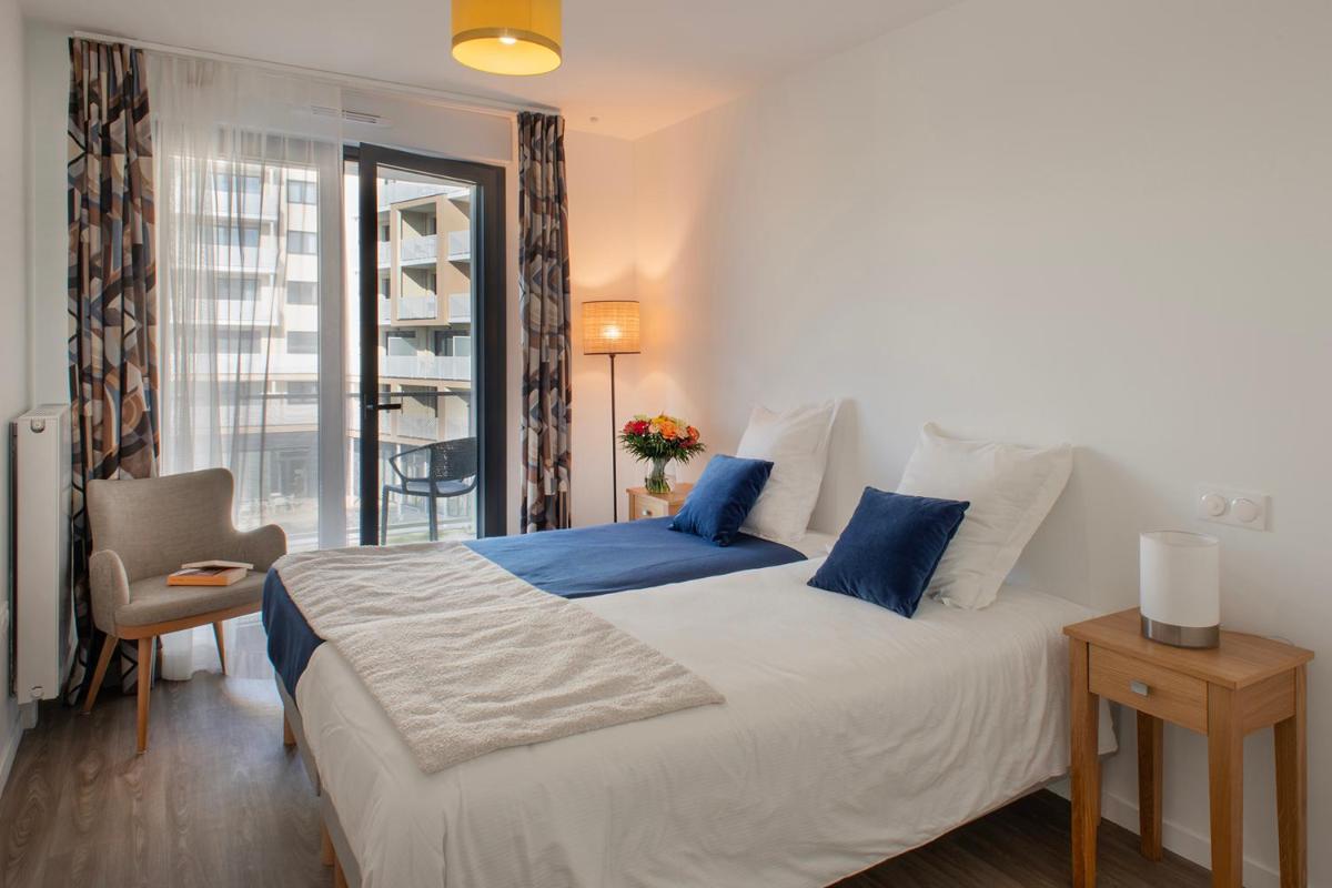 une chambre avec un grand lit blanc avec des oreillers bleus dans l'établissement DOMITYS L'ALLIACEE - Résidence Services Séniors, à Achères