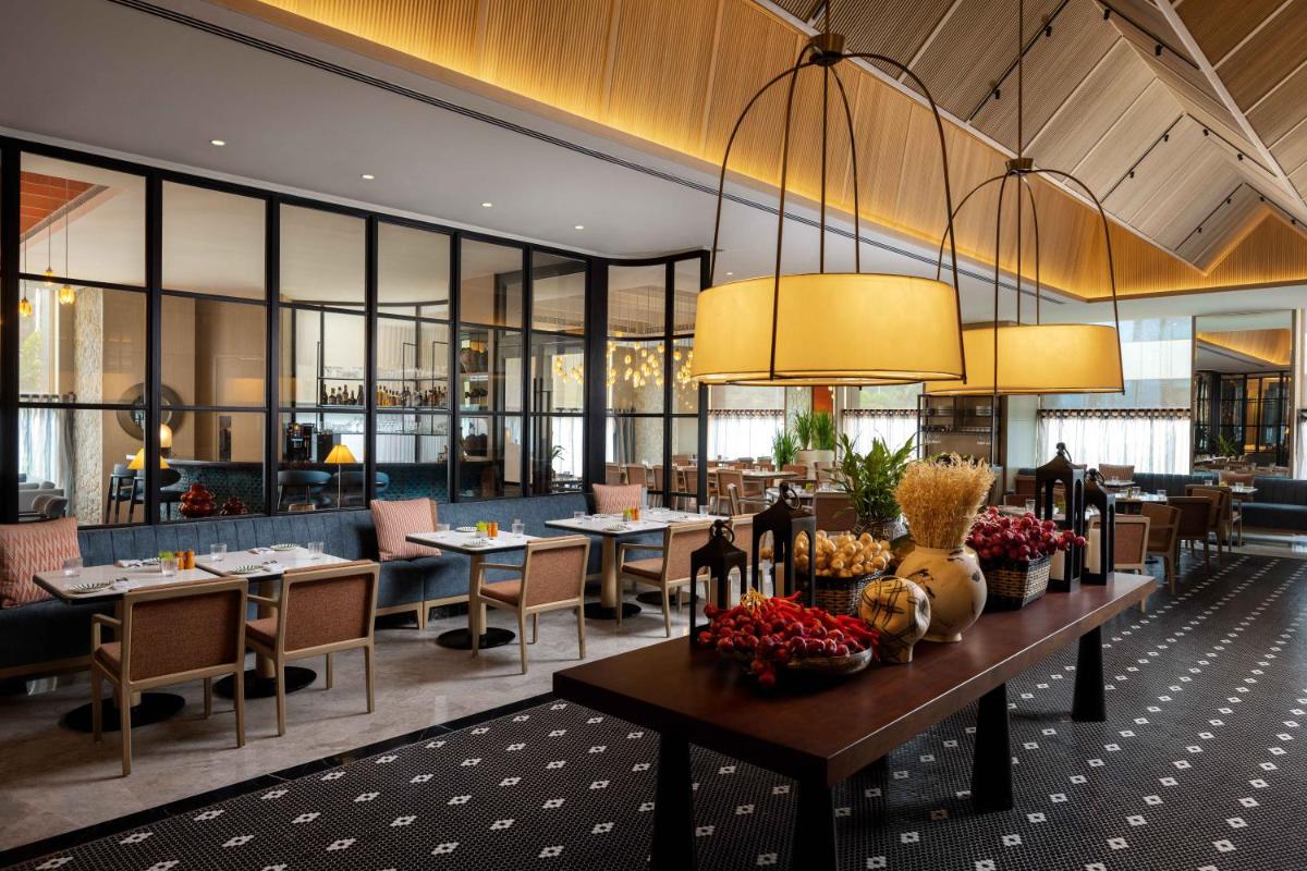 a restaurant with tables and chairs and large windows at Pullman Chennai Anna Salai - Premium Brand By Accor in Chennai