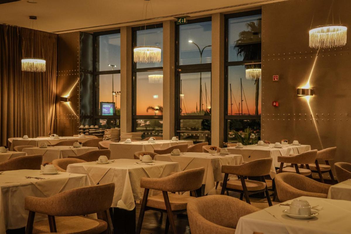 um restaurante com mesas, cadeiras e janelas brancas em Real Marina Hotel & Spa em Olhão