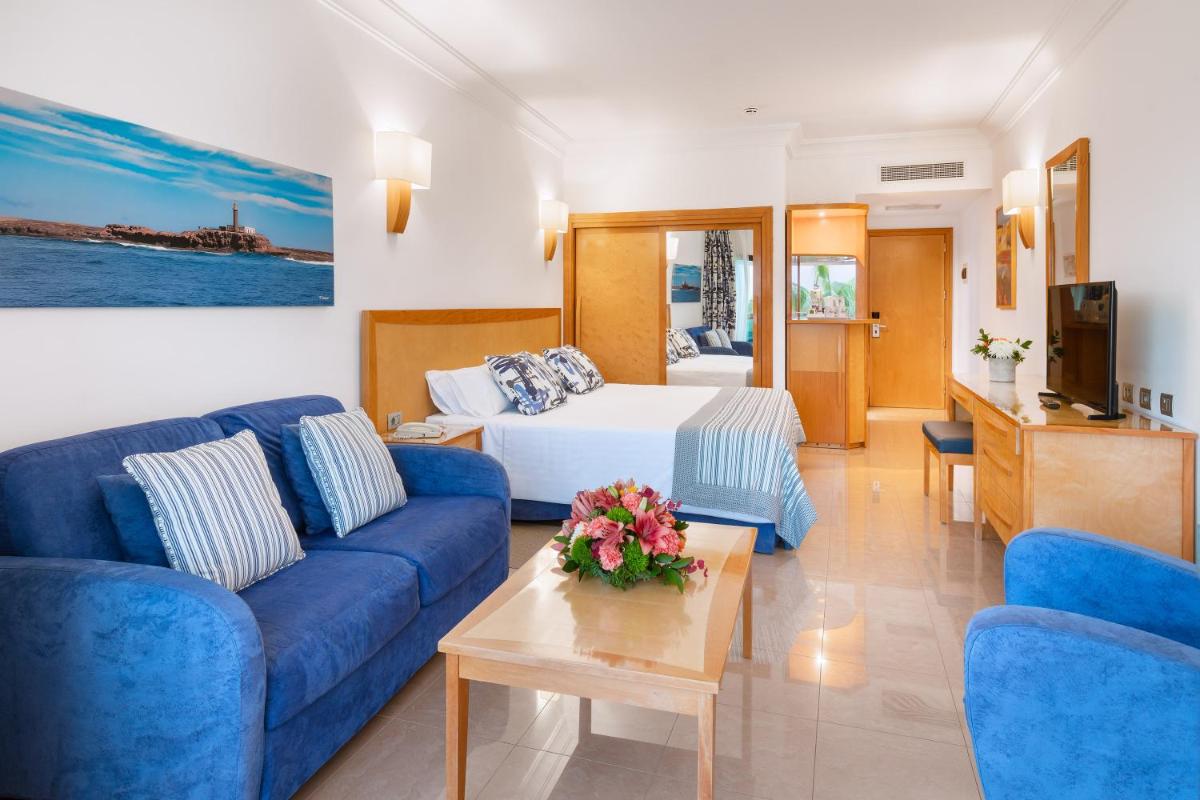 Una sala de estar con un sofá azul y una cama. en MUR Faro Jandia Fuerteventura & Spa, en Morro del Jable