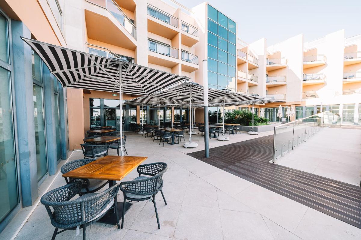 um pátio com uma mesa de madeira e cadeiras sob um guarda-sol em Real Marina Hotel & Spa em Olhão