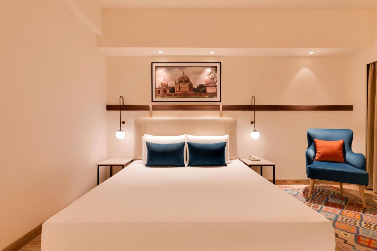 a bedroom with a bed and a blue chair at Lemon Tree Premier Hitec City Hyderabad in Hyderabad
