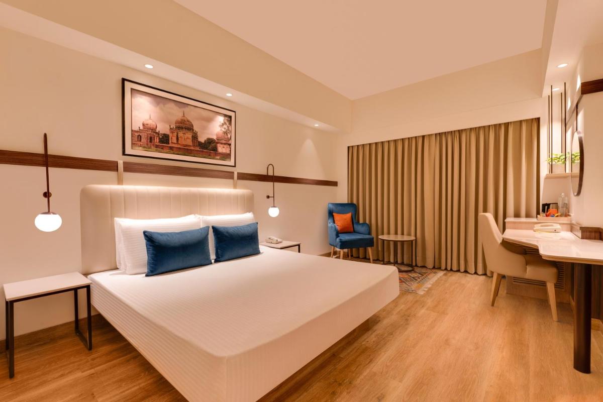 a bedroom with a white bed with blue pillows and a desk at Lemon Tree Premier Hitec City Hyderabad in Hyderabad