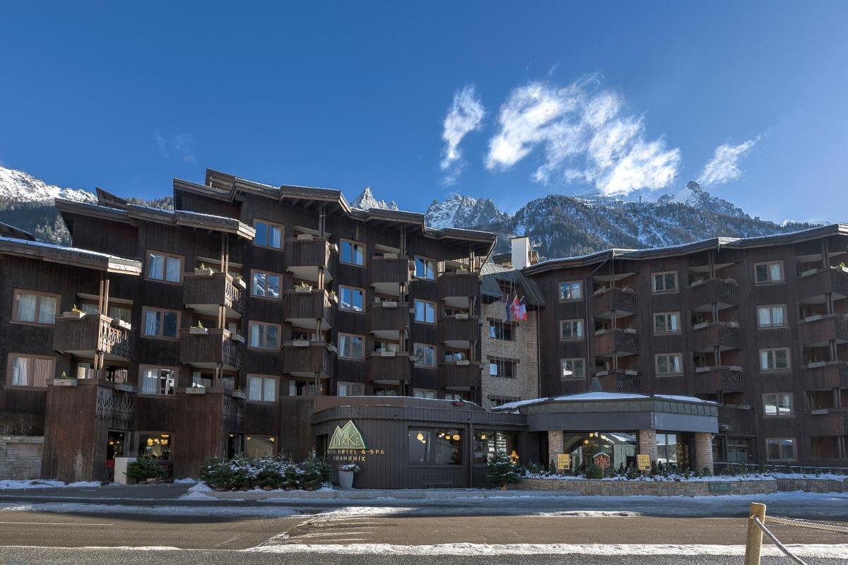 un grand immeuble avec des montagnes en arrière-plan dans l'établissement Lykke Hôtel & Spa Chamonix - ex Mercure, à Chamonix-Mont-Blanc