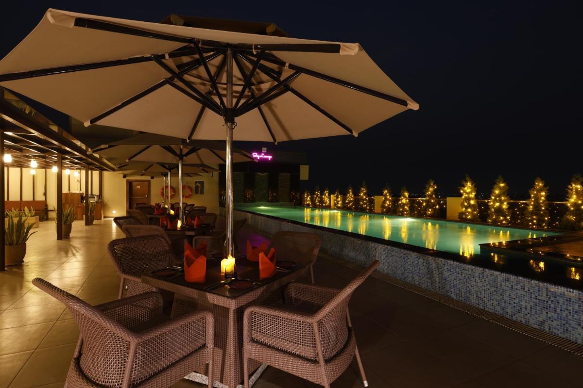 a table with an umbrella next to a swimming pool at night at Regenta Dehradun by Royal Orchid Hotels Limited in Dehradun
