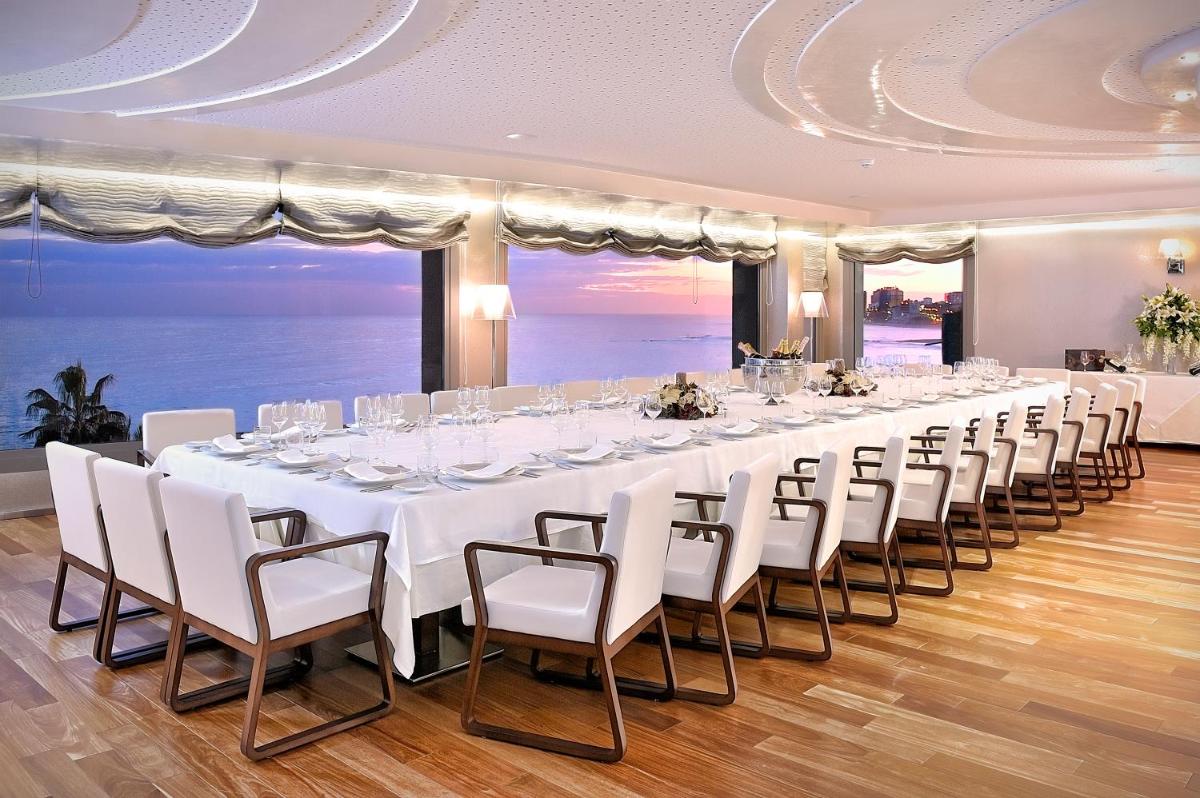 Una mesa larga con mesas y sillas blancas en una habitación con vista al mar. en Vincci Selección Aleysa, en Benalmádena