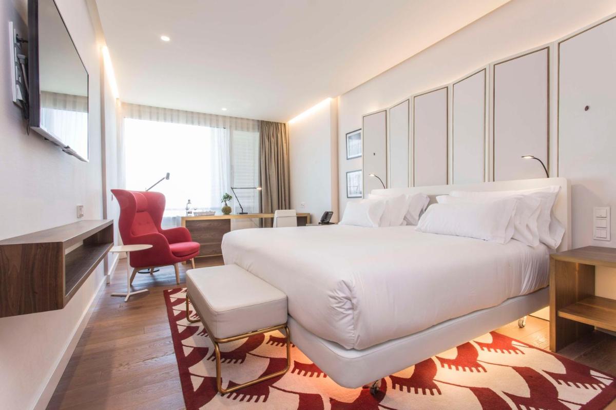 Un dormitorio con una gran cama blanca y una silla roja. en NH Collection Madrid Eurobuilding, en Madrid