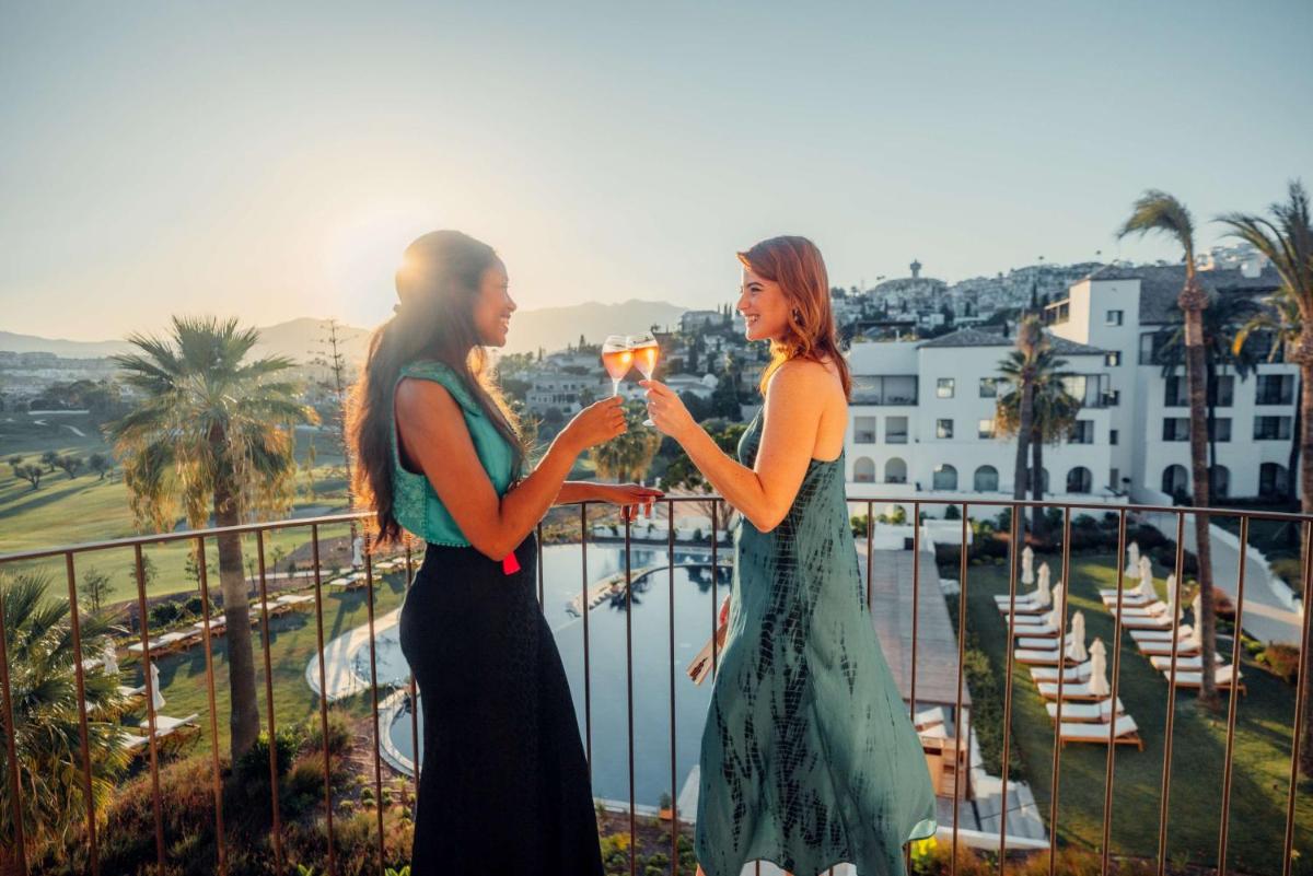 Dos mujeres de pie en un balcón con copas de vino. en La Zambra Resort Mijas - Marbella - The Unbound Collection by Hyatt, en Mijas