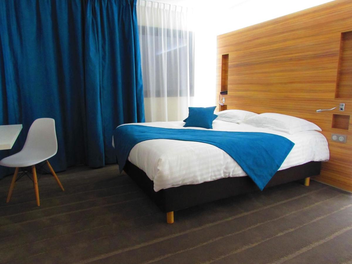 une chambre avec un grand lit avec des rideaux bleus dans l'établissement Brit Hotel & Spa Saint Brieuc Plérin, à Plérin