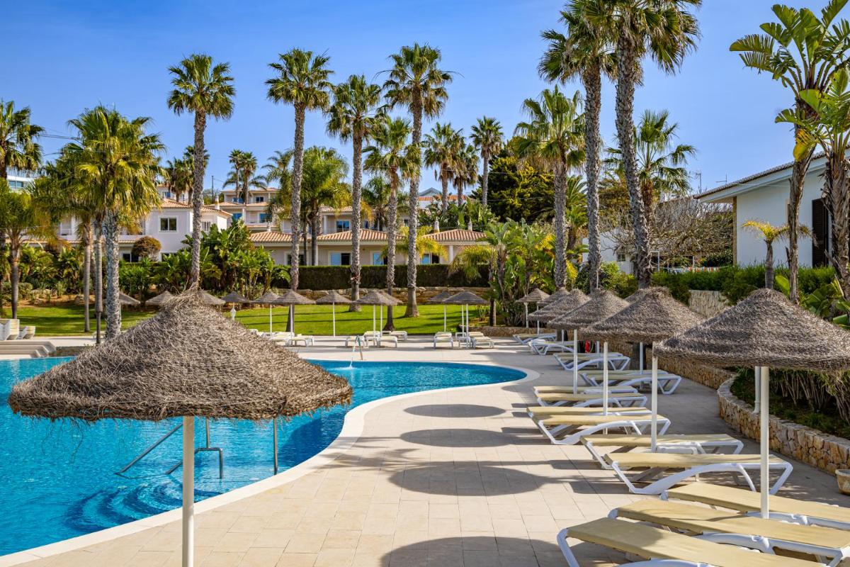 uma piscina de resort com cadeiras, guarda-sóis e palmeiras em Clube Porto Mos - Sunplace Hotels & Beach Resort em Lagos