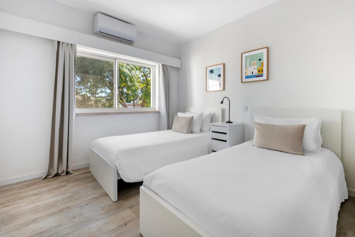 duas camas em um quarto branco com janela em Vilar do Golf na Quinta do Lago