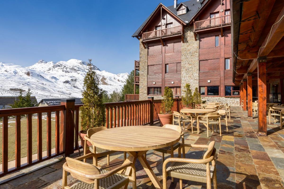 Un patio con mesas y sillas en un balcón con montañas. en Hotel Saliecho, en Formigal