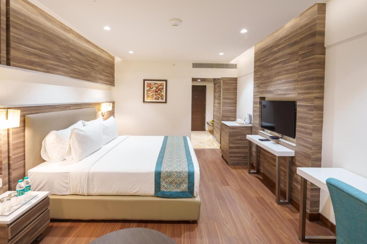 a hotel room with a bed and a flat screen tv at Pharos Hotels in Chennai
