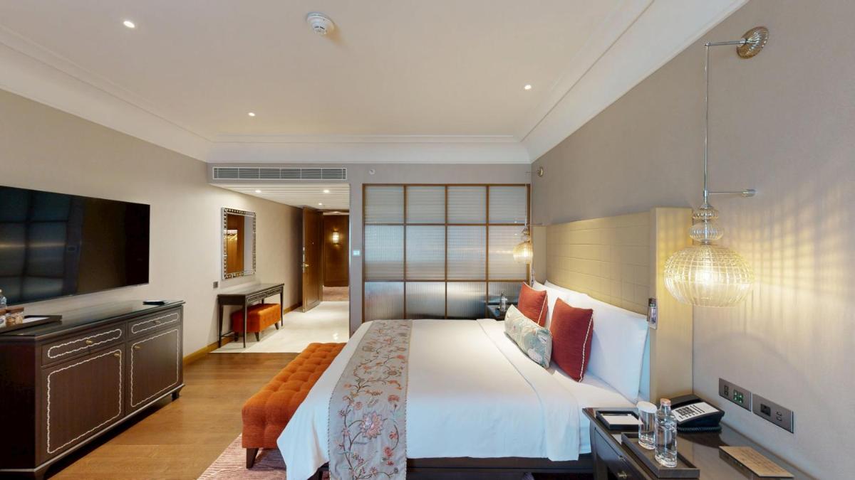 a bedroom with a large white bed and a desk at The Leela Hyderabad Banjara Hills in Hyderabad