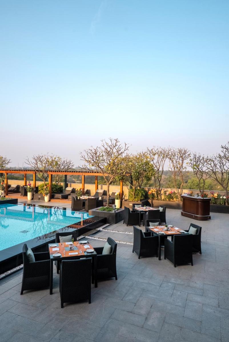 a patio with tables and chairs next to a swimming pool at The Leela Ambience Gurugram Hotel & Residences - The Luxury Urban Sanctuary in Gurgaon