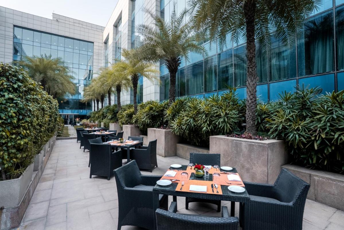 a restaurant with tables and chairs and palm trees at The Leela Ambience Gurugram Hotel & Residences - The Luxury Urban Sanctuary in Gurgaon