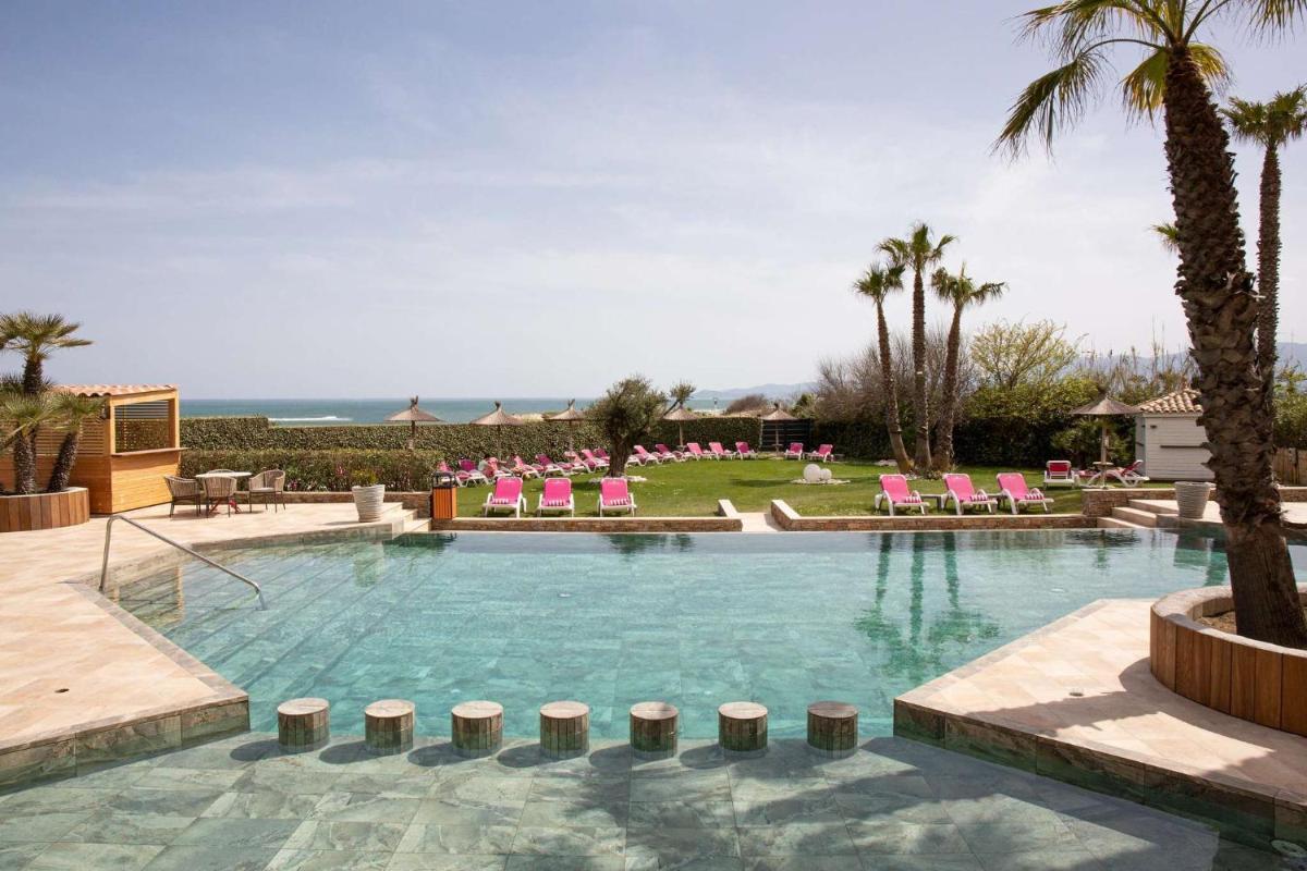 une grande piscine avec des chaises roses et des palmiers dans l'établissement Grand Hôtel Les Flamants Roses Thalasso & Spa, à Canet