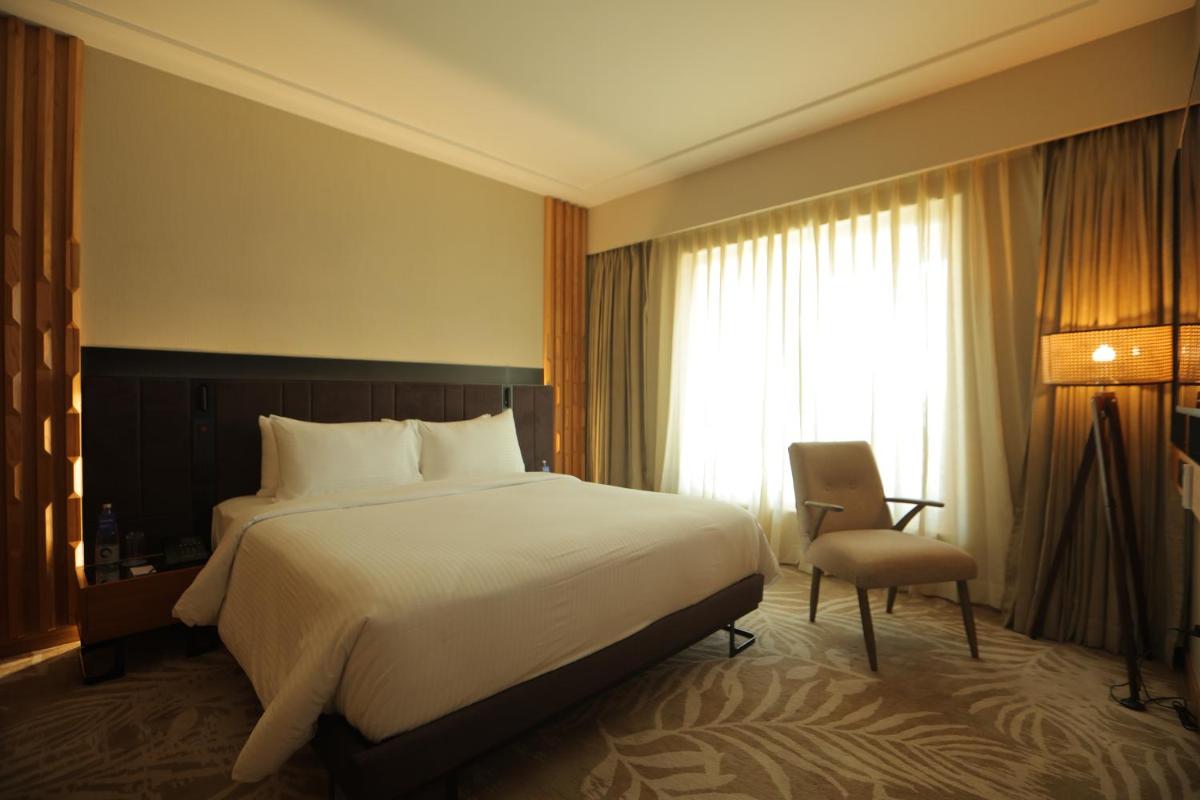 a bedroom with a bed and a chair and a window at Novotel Hyderabad Airport in Hyderabad