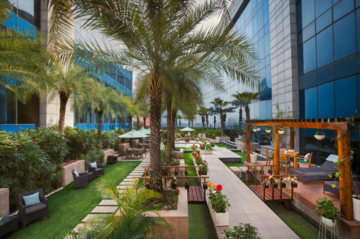 an outdoor patio with tables and palm trees in a building at The Leela Ambience Gurugram Hotel & Residences - The Luxury Urban Sanctuary in Gurgaon