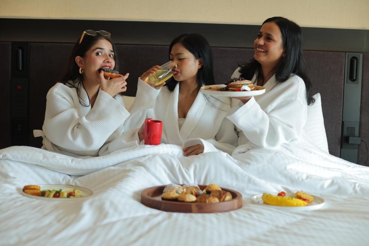 three women sitting in a bed eating food at Novotel Hyderabad Airport in Hyderabad