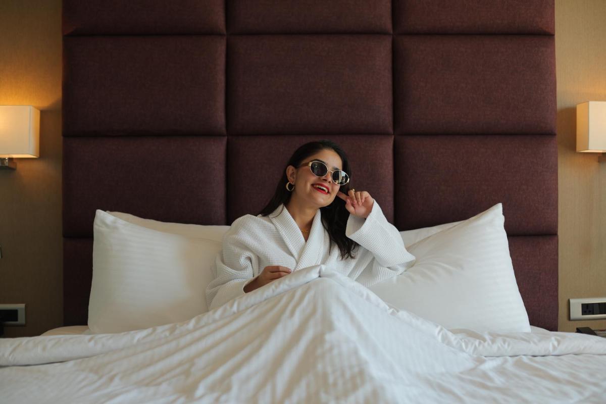 a woman in a white robe sitting on a bed at Novotel Hyderabad Airport in Hyderabad