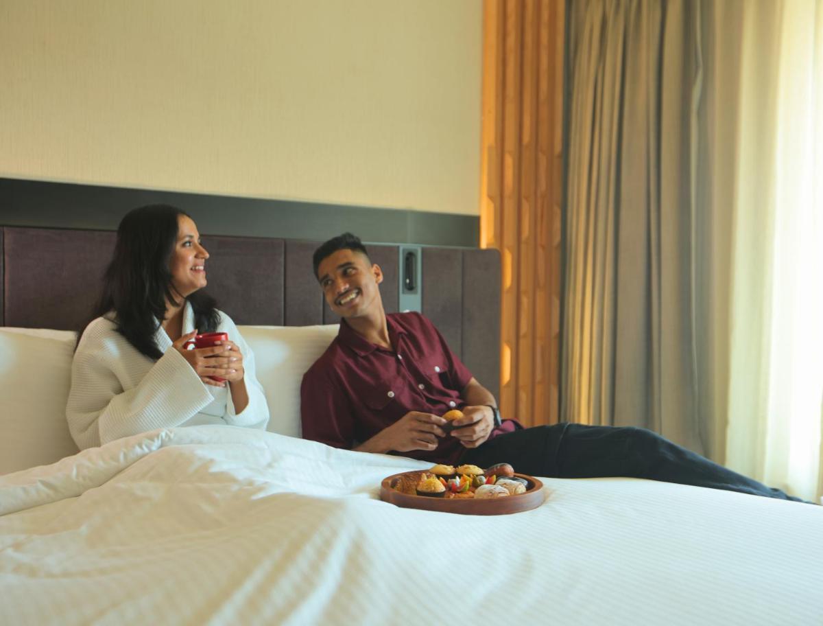 a man and woman sitting on a bed with a plate of food at Novotel Hyderabad Airport in Hyderabad