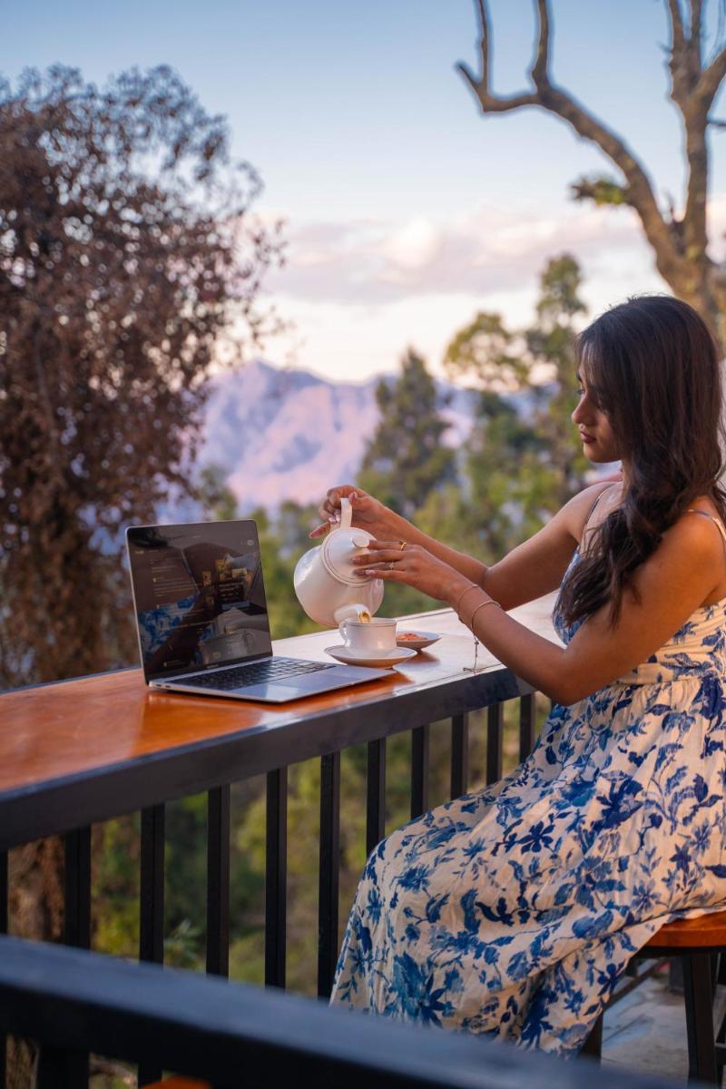 a woman sitting at a table with a tea pot and a laptop at Perfectstayz Premium Westend at Mall Road in Mussoorie