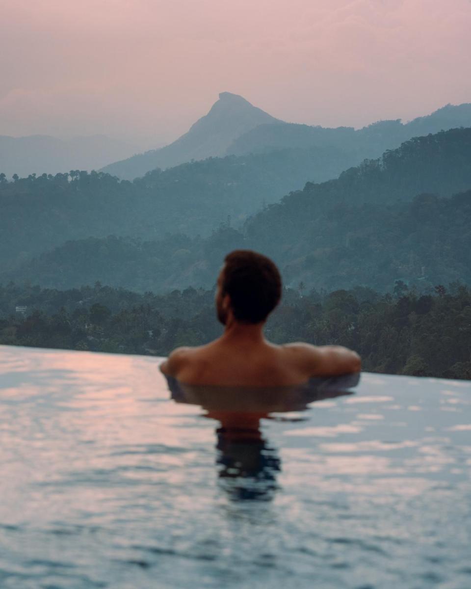 a man in a body of water with mountains in the background at The Panoramic Getaway in Munnar
