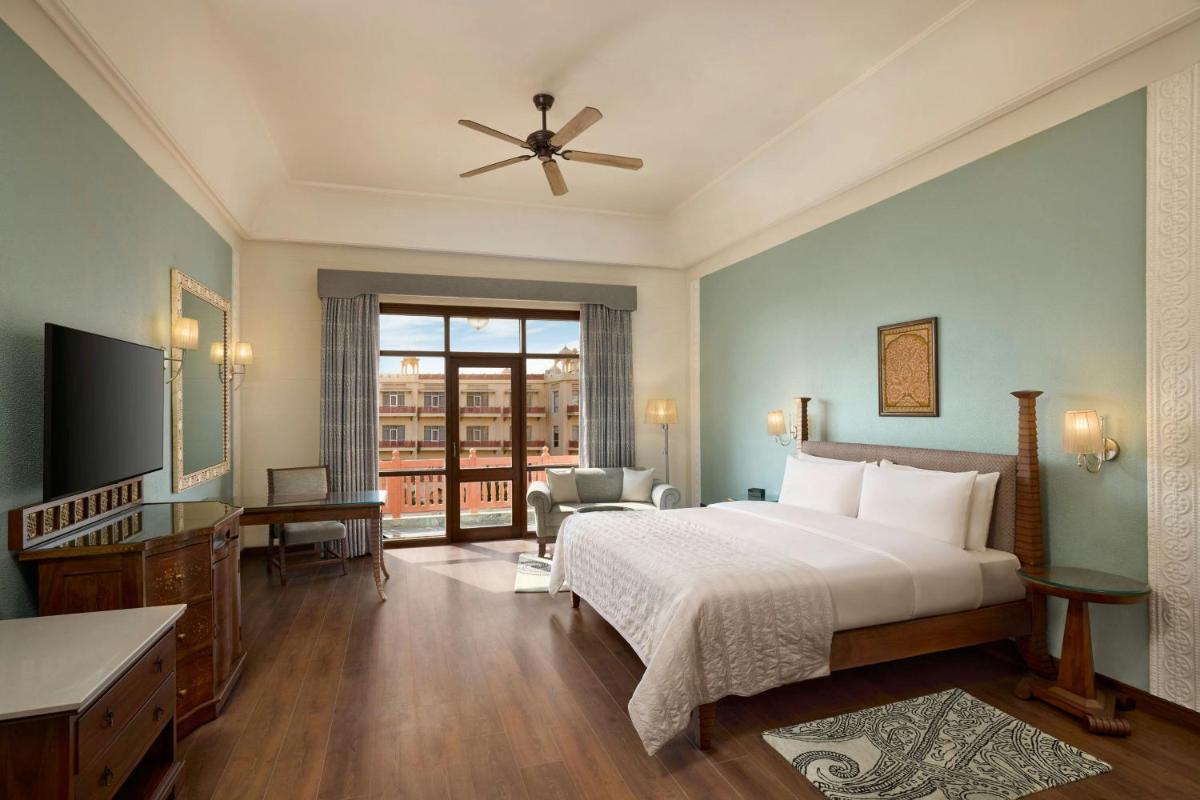 a bedroom with a bed and a large window at Le Meridien Jaipur Resort & Spa in Jaipur