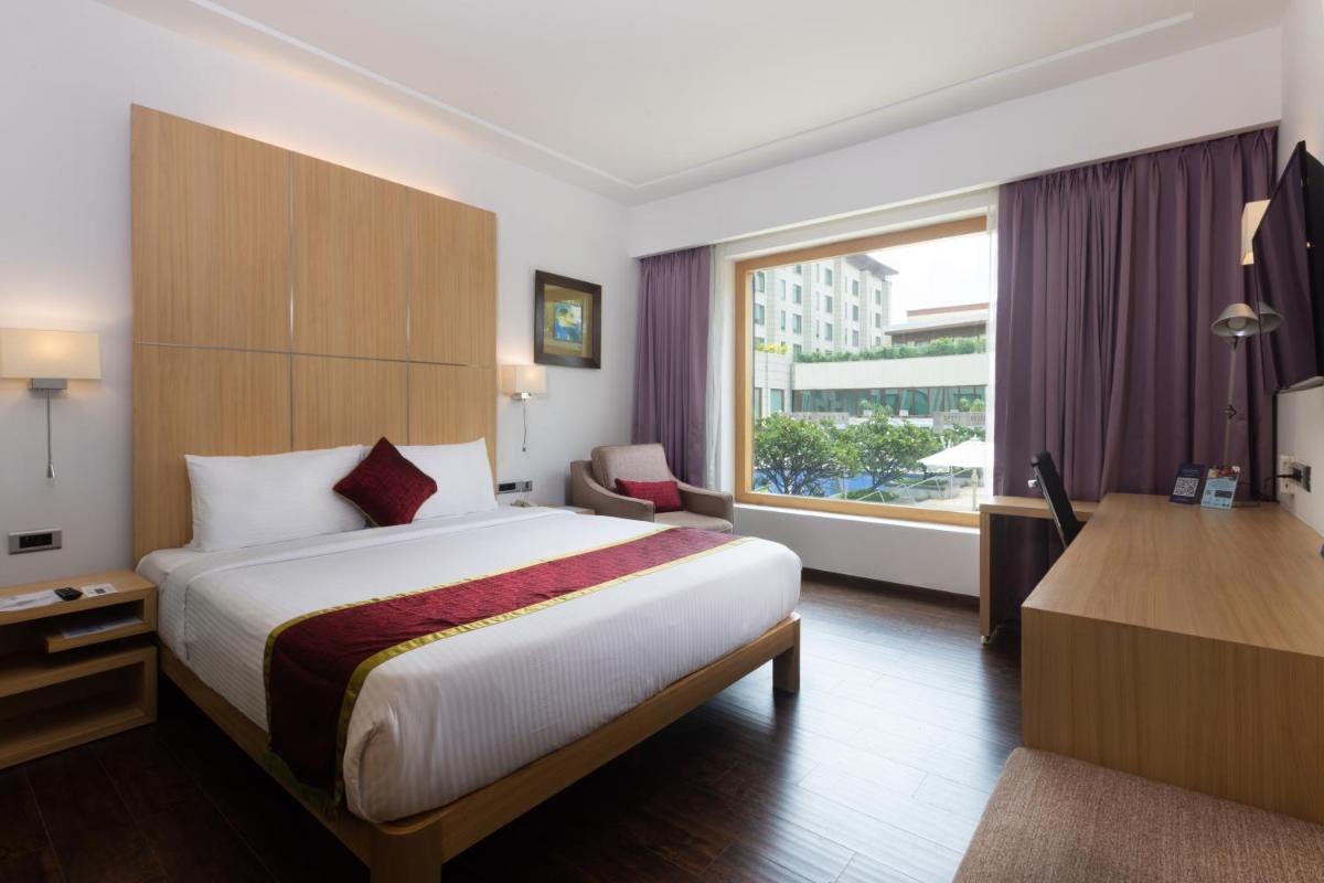 a hotel room with a bed and a desk and a window at Novotel Hyderabad Airport in Hyderabad
