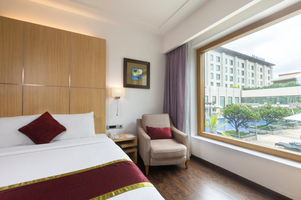 a bedroom with a bed and a window and a chair at Novotel Hyderabad Airport in Hyderabad