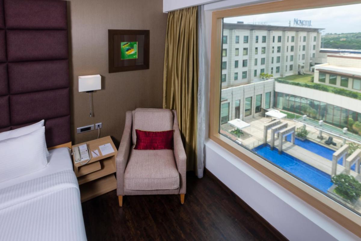a hotel room with a chair and a large window at Novotel Hyderabad Airport in Hyderabad