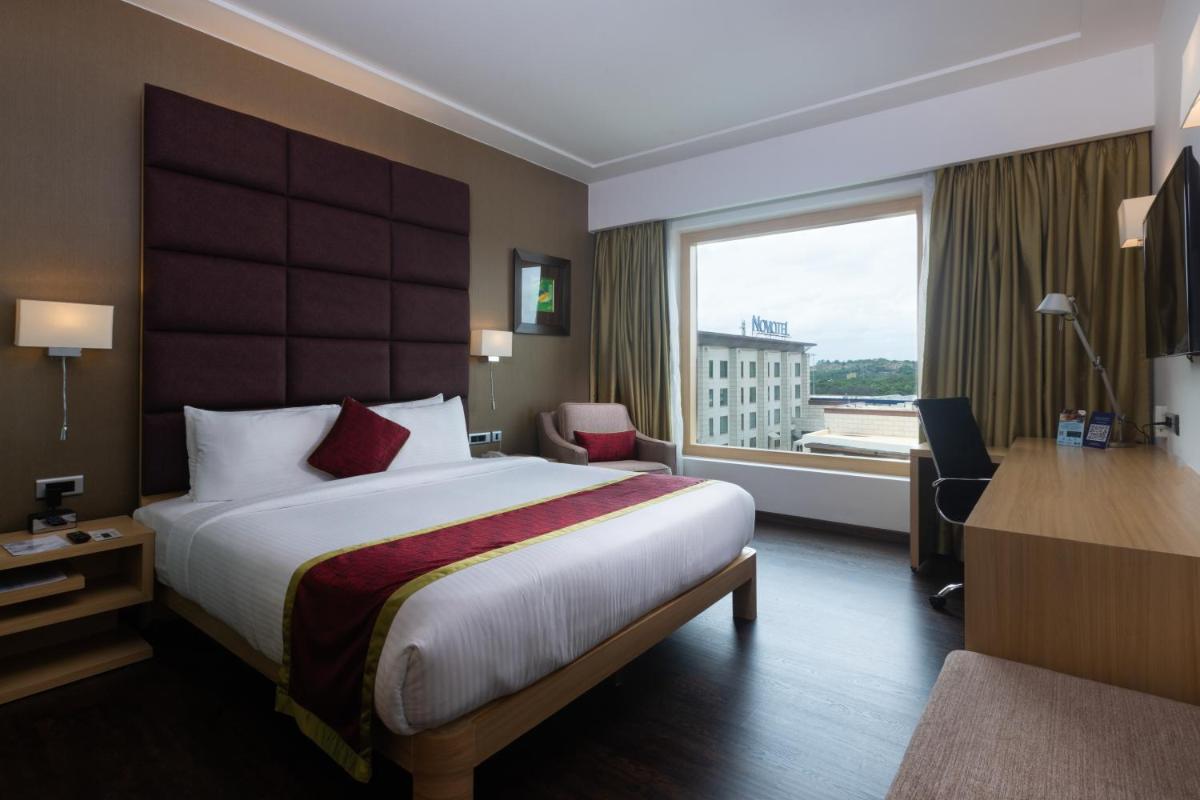 a hotel room with a bed and a desk and a window at Novotel Hyderabad Airport in Hyderabad