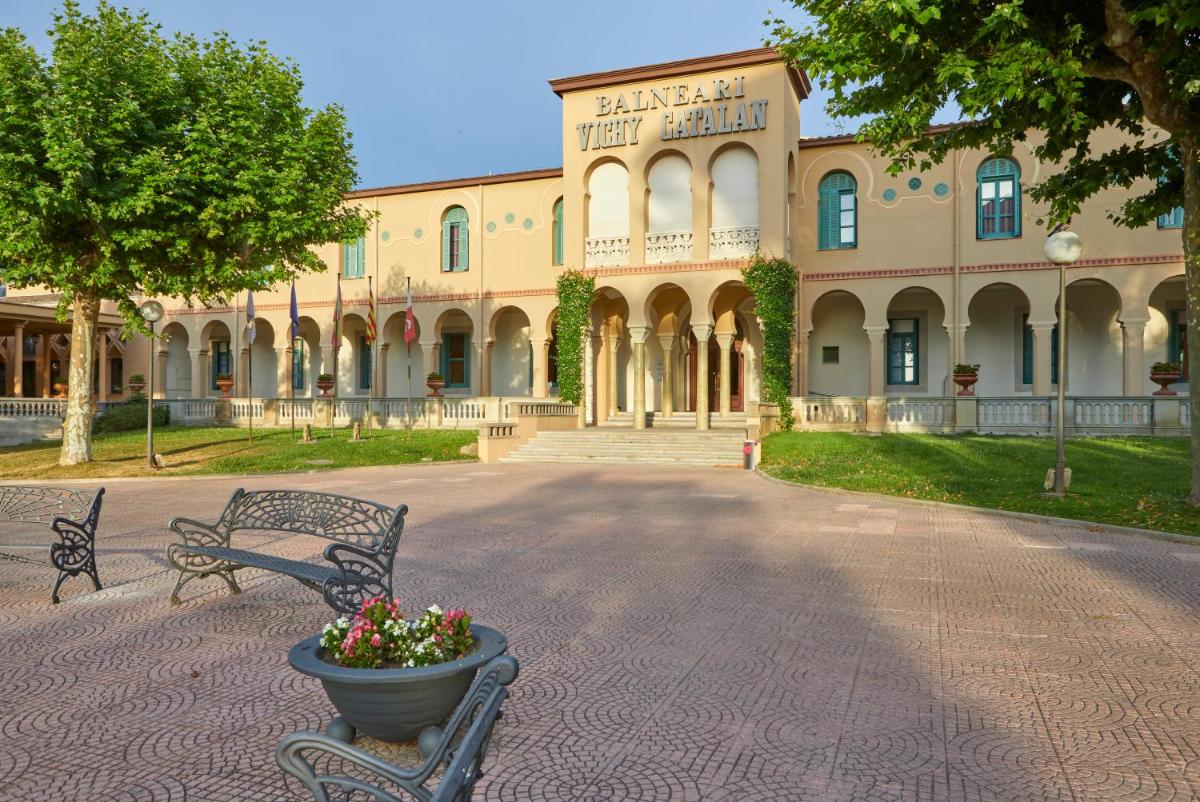 Dos bancos frente a un edificio con una maceta. en 1881 Hotel Balneario Vichy Catalan, en Caldes de Malavella