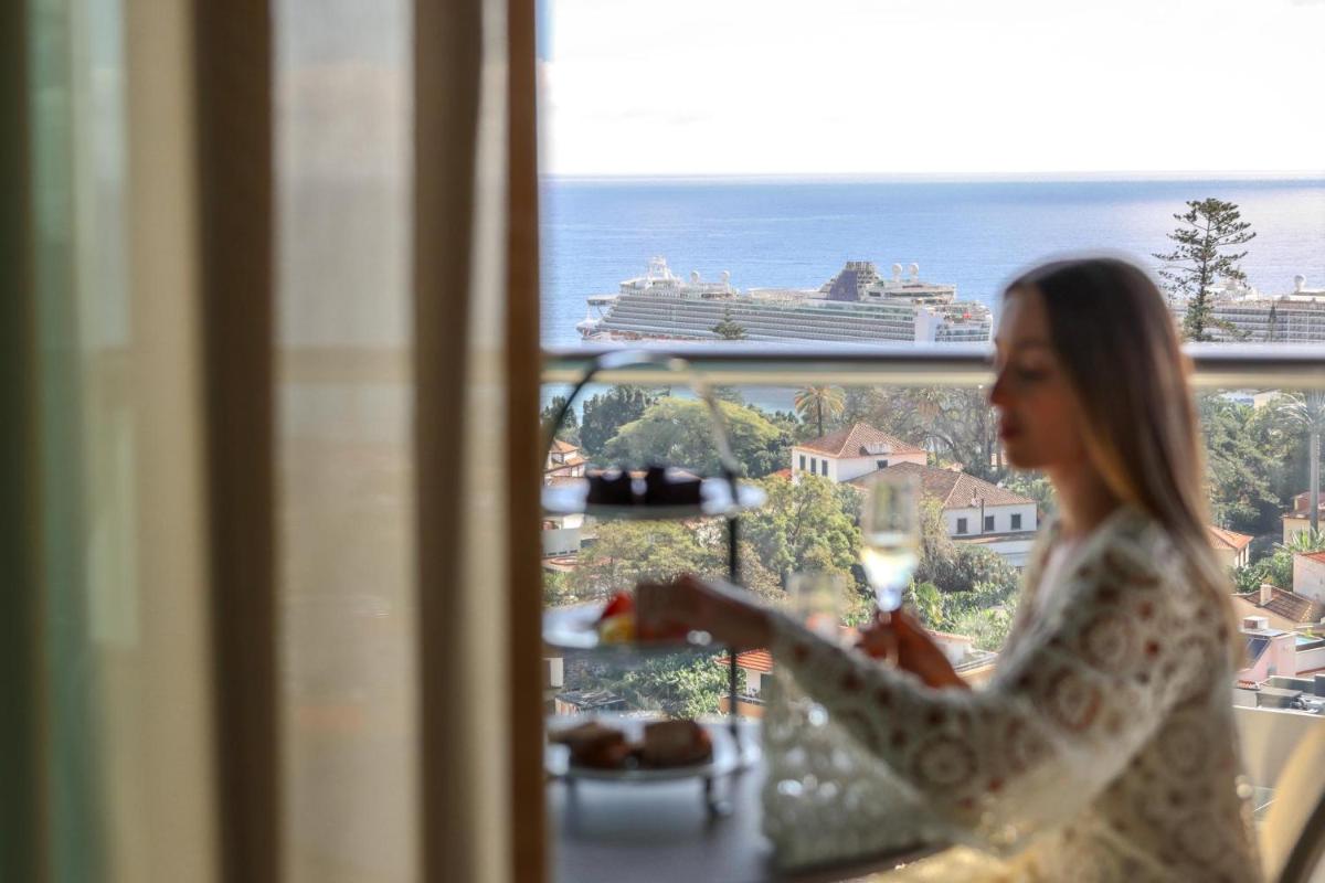 Uma mulher comendo em frente a uma janela com vista para um navio de cruzeiro. em The Views Baia - Adults Only no Funchal