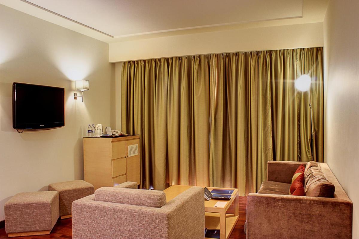a living room with a couch and two chairs and a television at Novotel Hyderabad Airport in Hyderabad