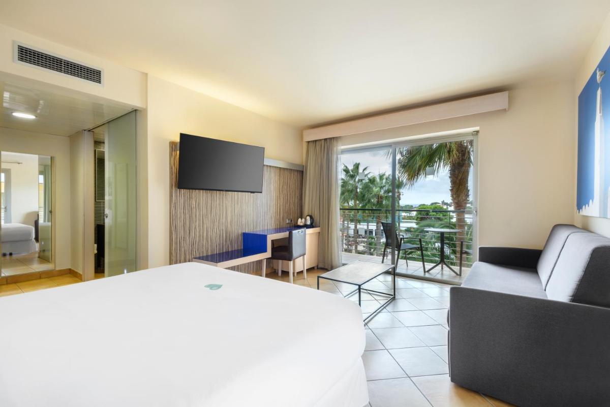 Un dormitorio con una cama y una sala de estar con televisión. en Occidental Menorca, en Punta Prima