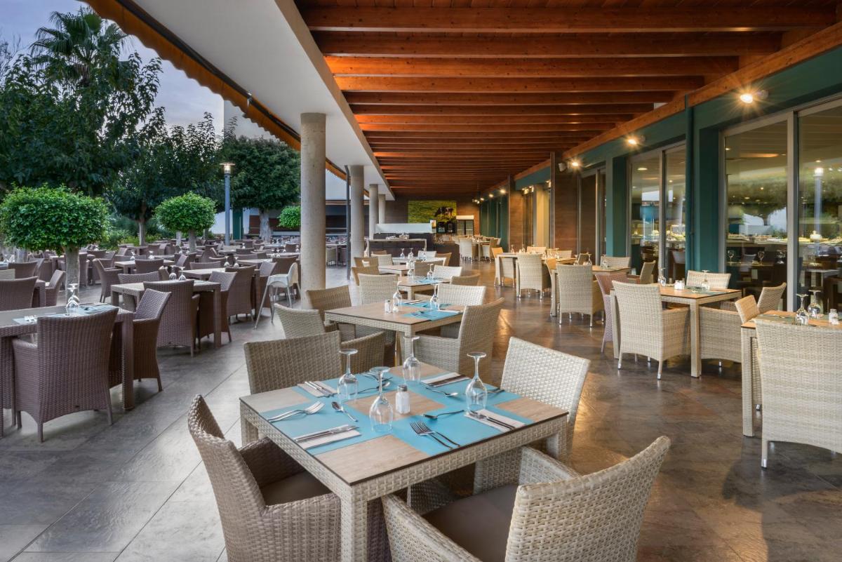 un restaurante al aire libre con mesas, sillas y mesa en Occidental Menorca, en Punta Prima