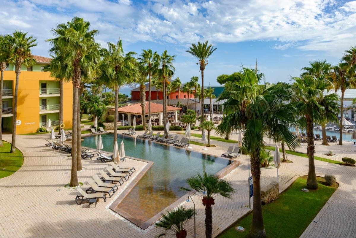 Una piscina tipo resort con tumbonas y palmeras. en Occidental Menorca, en Punta Prima
