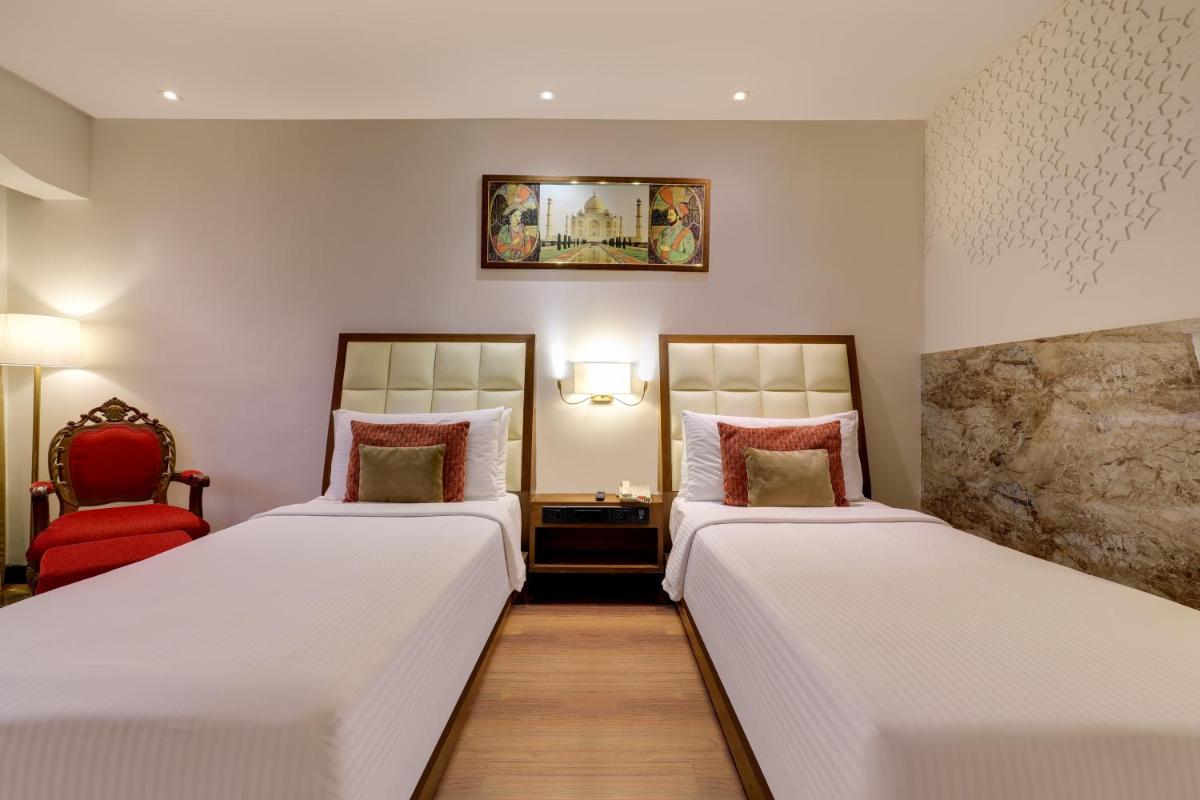 a hotel room with two beds and a red chair at Saura Hotel, Agra - A Club Mahindra Associate in Agra